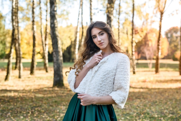 Mujer joven con vestido verde de moda caminando en el parque de otoño.