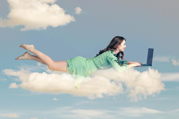 Mujer joven en vestido volando con laptop en el cielo