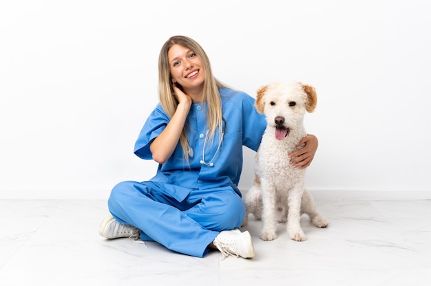 Mujer joven veterinario con perro sentado en el suelo riendo