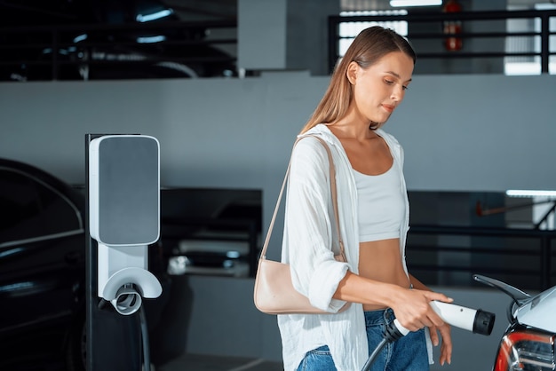 Foto mujer joven viaja con un coche eléctrico eléctrico a las entrañas del estacionamiento del centro comercial