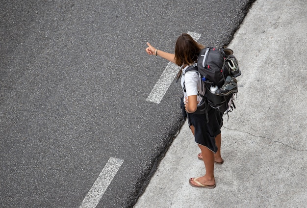 Mujer joven viaja haciendo autostop cerca de una carretera