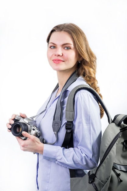 Mujer joven viajera con cámara y mochila sobre fondo blanco.