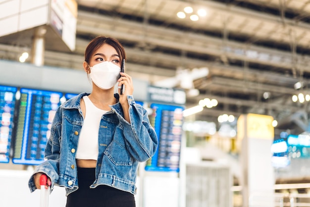 Mujer joven viajera en cuarentena por coronavirus con máscara quirúrgica protección facial con equipaje mira viaje de vuelo antes de un largo viaje de vacaciones en el aeropuerto de la terminal internacional