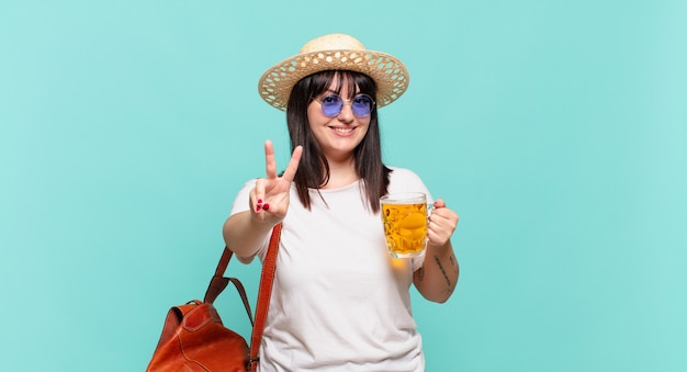 Mujer joven viajera sonriendo y mirando feliz, despreocupada y positiva, gesticulando victoria o paz con una mano