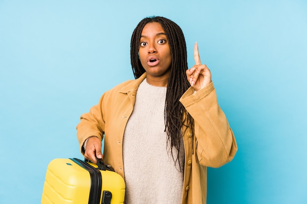 Mujer joven del viajero afroamericano que sostiene una maleta aislada teniendo una gran idea, concepto de creatividad.