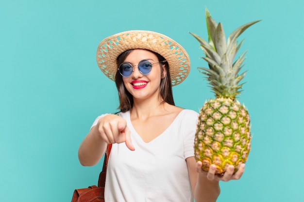 Mujer joven viajero apuntando o mostrando y sosteniendo una piña