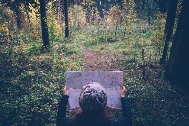 Mujer joven del viajero con el mapa, en el bosque del verde del otoño en día soleado.