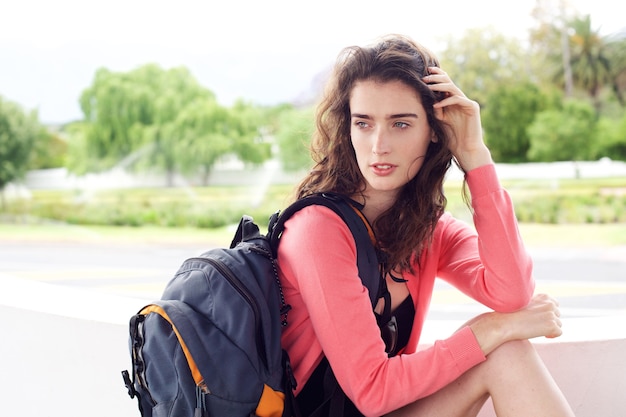 Mujer joven viajero sentado afuera esperando con bolsa