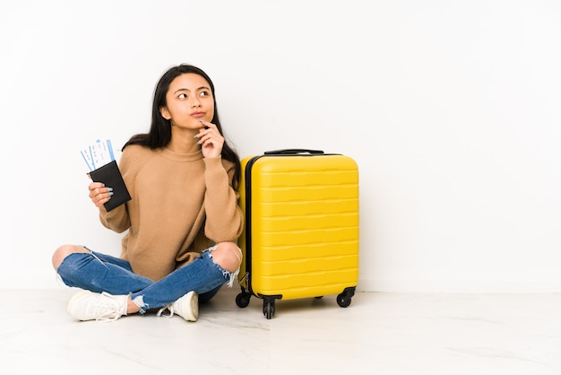Mujer joven viajero sittting en el suelo con una maleta haciendo un plan en mente, creando una idea.