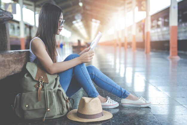 Mujer joven de los viajeros con la mochila que parece sostener un mapa en la estación de tren. Día del turismo