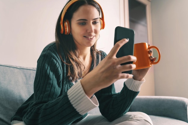 Mujer joven viendo contenido en línea desde el teléfono inteligente sentado en el sofá en casa