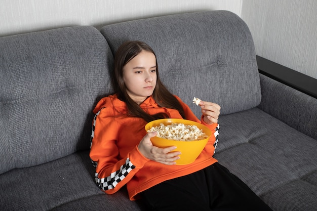 Mujer joven viendo un programa poco interesante en la televisión con palomitas de maíz en sus manos