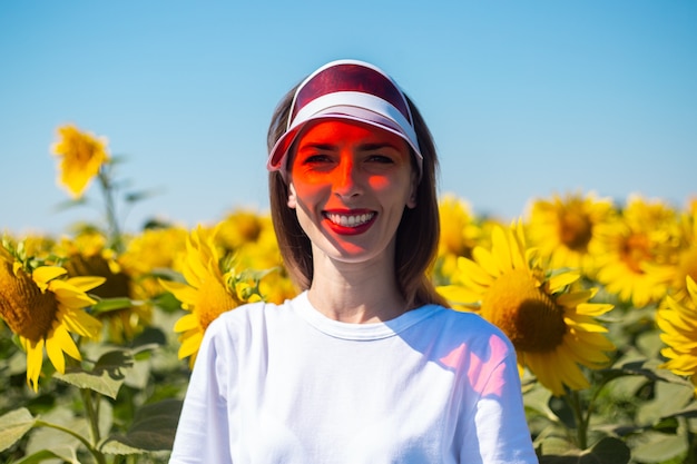 Mujer joven con visera roja y camiseta blanca en campo de girasol.