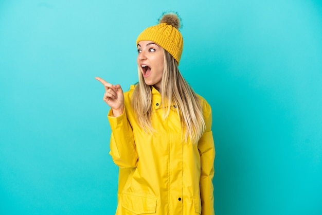 Mujer joven vistiendo un abrigo impermeable sobre fondo azul aislado con la intención de darse cuenta de la solución mientras levanta un dedo hacia arriba