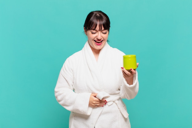 Mujer joven vistiendo albornoz riéndose a carcajadas de una broma hilarante, sintiéndose feliz y alegre, divirtiéndose