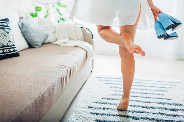 Mujer joven vistiendo bata de seda y sosteniendo zapatos azules en casa, novia el día de la boda