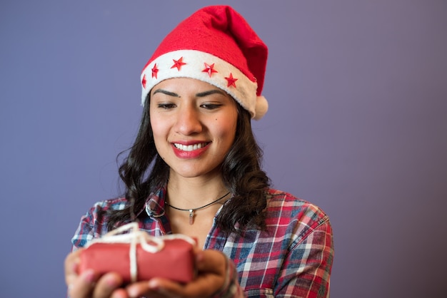 Mujer joven vistiendo un gorro de Papá Noel viendo su pequeño regalo de Navidad