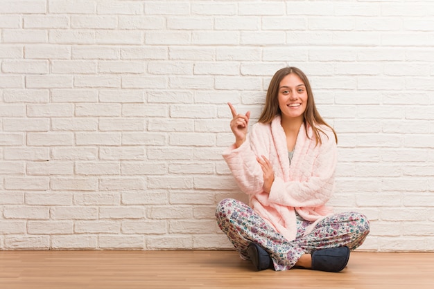 Mujer joven vistiendo pijama apuntando hacia un lado con el dedo