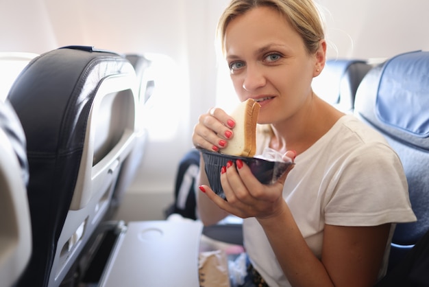 Mujer joven volando en avión y comiendo sándwich