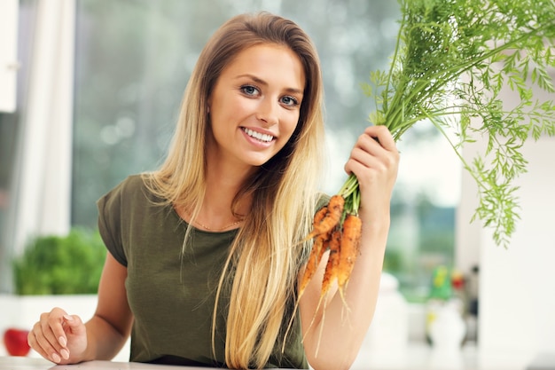 Mujer joven con zanahorias frescas en la cocina