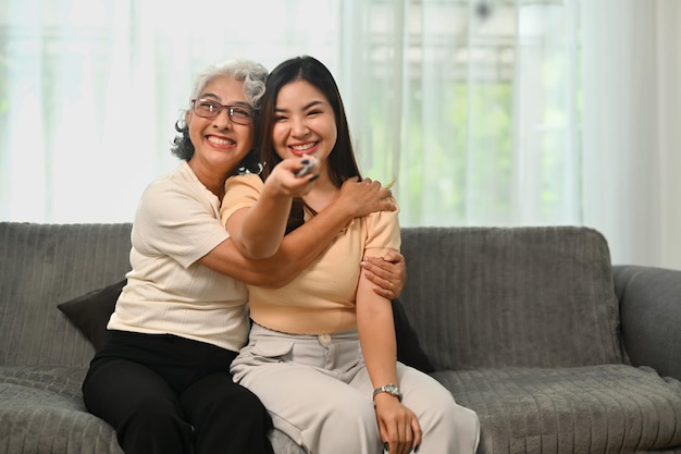 Mujer jubilada alegre relajándose en el sofá con su hija adulta y viendo televisión el fin de semana