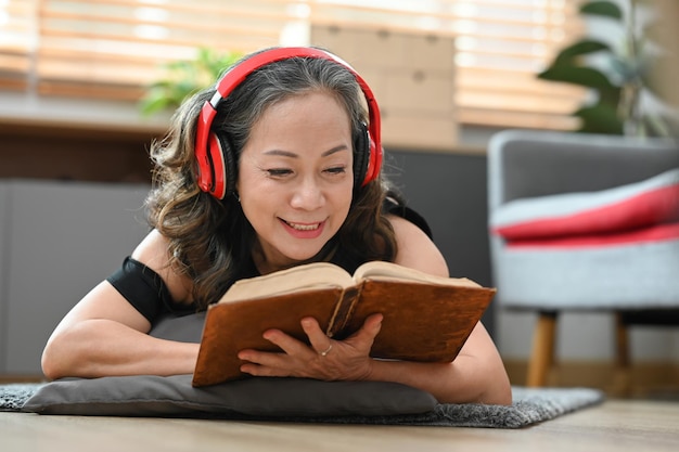 Mujer jubilada feliz escuchando música en auriculares y leyendo libros en casa