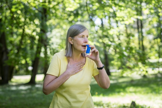 Mujer jubilada mayor con asma respirando un inhalador en un parque de verano