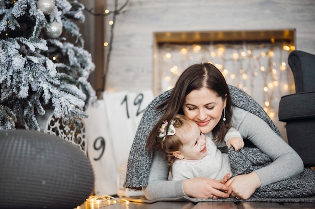 La mujer juega con su hija antes de un árbol de Navidad