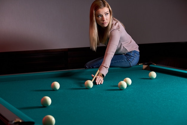 Mujer jugando al juego de billar, preparándose con el objetivo de disparar bolas de billar en una mesa de billar, sentado en él