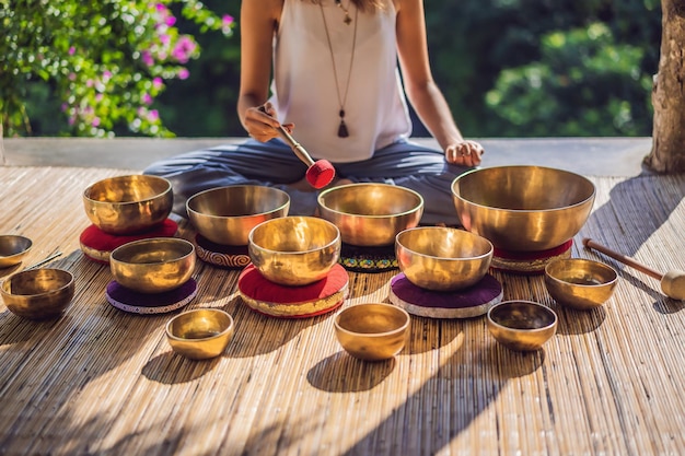 Mujer jugando en un cuenco tibetano mientras está sentado en una estera de yoga contra una cascada