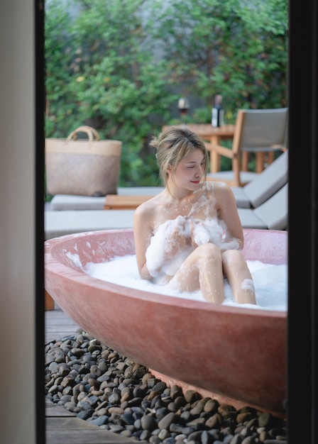 Mujer jugando con espuma de burbujas mientras toma un baño en la bañera.
