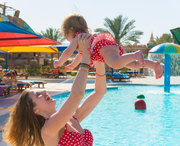 Mujer jugando con una niña divertida mientras está de pie en la piscina en el parque acuático en un día soleado en el resort