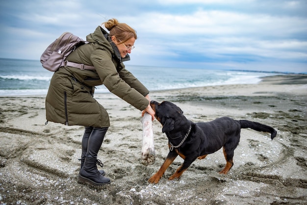 Mujer jugando con perro rottweiler en clima frío en la playa