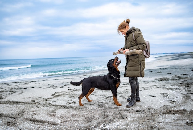 Mujer jugando con perro rottweiler en clima frío en la playa