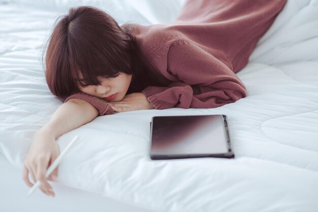 Una mujer jugando una tableta en la cama en un dormitorio blanco