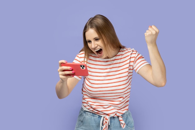 Mujer jugando en el teléfono inteligente ganando el puño cerrado celebrando su victoria