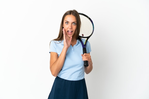 Mujer jugando tenis sobre pared blanca aislada con sorpresa y expresión facial conmocionada