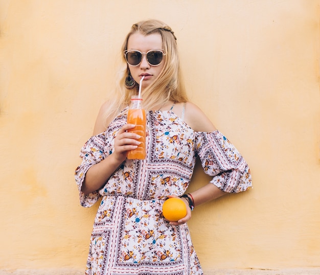 Mujer con jugo y naranja en la pared