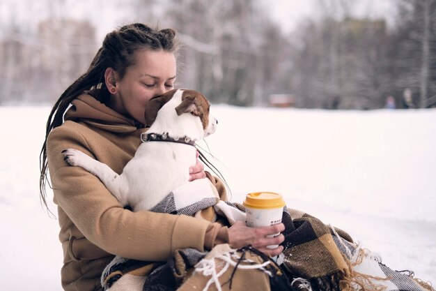 Mujer juguetona con perro elegante mujer hipster abrazando y sonriendo lindo cachorro en el parque de invierno frío y nevado momentos de verdadera felicidad