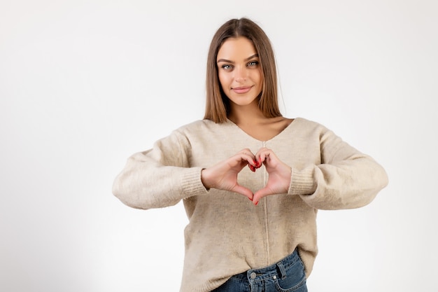 Foto mujer juguetona que muestra gesto del corazón con las manos aisladas sobre blanco