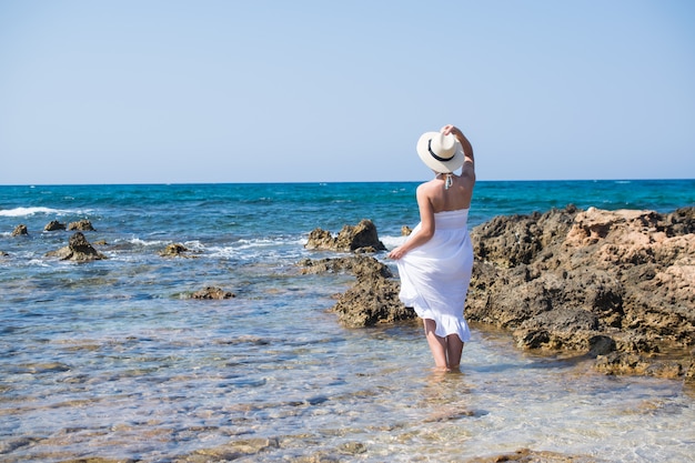 Mujer junto al mar con un vestido blanco en un día soleado