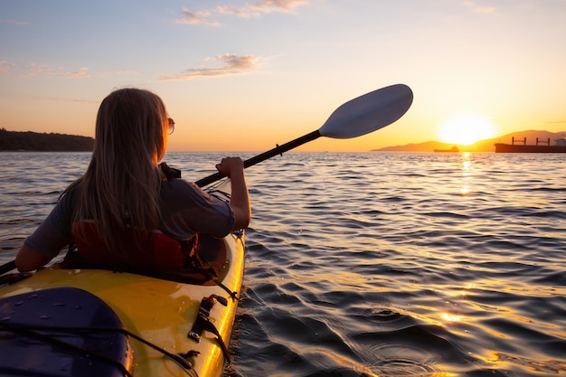 Foto mujer en un kayak está remando en el océano durante una puesta de sol vibrante