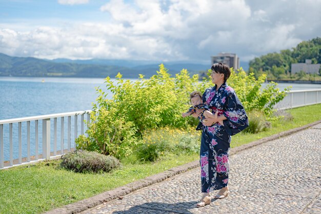 Una mujer con un kimono se encuentra en un camino empedrado con un lago al fondo.