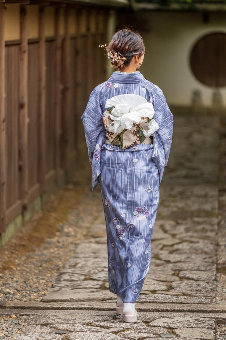 una mujer en kimono con una flor en la espalda camina por un camino de piedra
