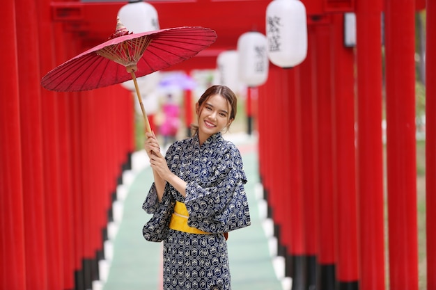 una mujer en kimono con paraguas caminando hacia el santuario, en el jardín japonés.