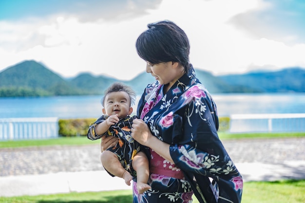 Una mujer con kimono sostiene a un bebé frente a un lago.