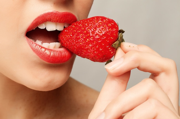 Mujer con labios rojos comiendo fresa