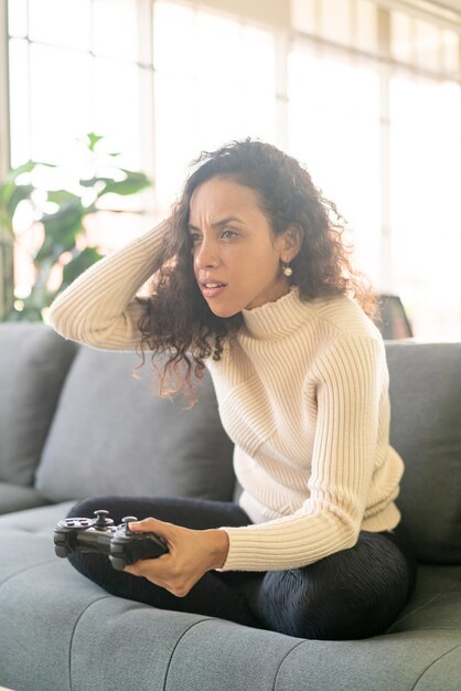 Mujer Laitin jugando videojuegos con las manos sosteniendo el joystick en el sofá en casa