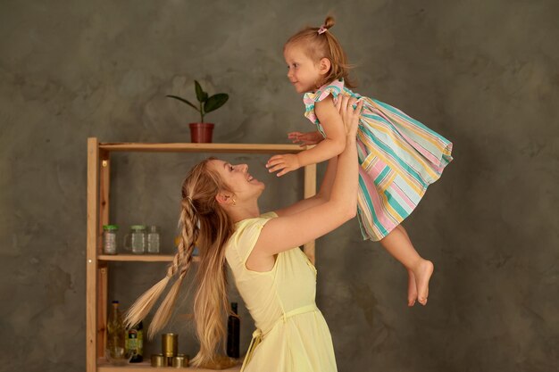 Mujer lanza a la niña al aire linda madre juega con la pequeña hija en la cocina