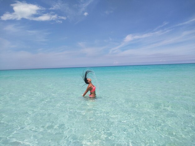 Mujer lanzando el cabello en el mar contra el cielo